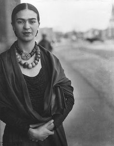 an old black and white photo of a woman with necklaces on her neck standing in front of a building