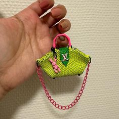 a hand holding a small purse with a chain around it and a pink handle on the end