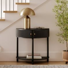 a round table with a lamp on top next to a stair case and potted plant