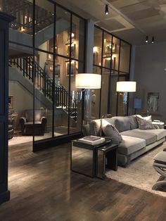 a living room filled with lots of furniture and large glass windows next to a stair case