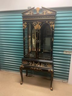 an antique black and gold china cabinet in front of a shuttered blue metal door