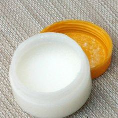 an orange and white container sitting on top of a beige cloth next to a small jar