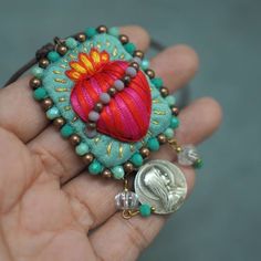 a hand holding a small beaded brooch with a coin in it's palm