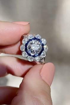 a close up of a person's hand holding a ring with a diamond and blue center