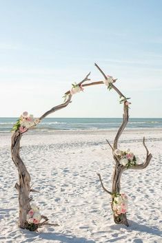 a wooden arch on the beach with flowers in it and a rainbow painted surfboard