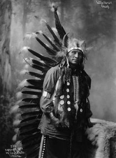 an old black and white photo of a native american man with feathers on his head