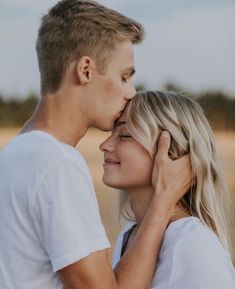 a young man and woman kissing each other in the middle of a desert field with grass