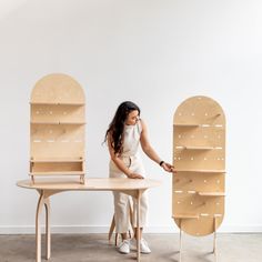 a woman standing next to a table with two wooden shelves on each side and one shelf behind her