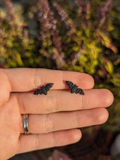 a person's hand with two rings on it and some plants in the background