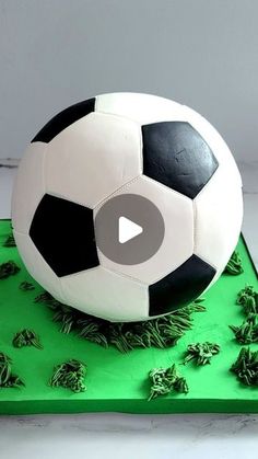 a soccer ball cake with green frosting and grass on the bottom, sitting on top of a table