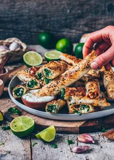 someone is picking up some food from a plate with limes and garlic on the side