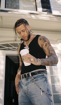 a man with tattoos holding a drink in front of a house