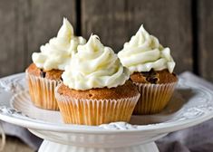 three cupcakes with white frosting on a cake plate