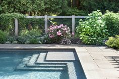 a pool surrounded by plants and flowers next to a fence