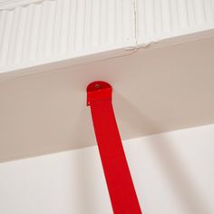 a red piece of tape is hanging from the ceiling in front of a white wall