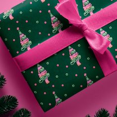 a present wrapped in green wrapping paper with pink ribbon on it and decorated with christmas trees