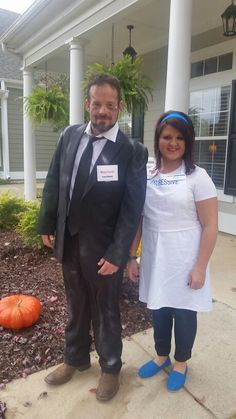 a man and woman standing in front of a house with pumpkins on the ground