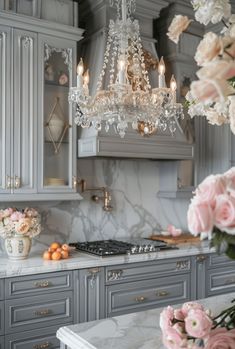 a chandelier hanging from the ceiling in a kitchen with gray cabinets and marble counter tops