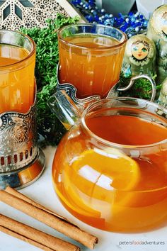 two glasses of orange juice with cinnamon sticks next to them on a white tablecloth