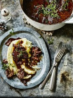 a plate with meat and mashed potatoes on it next to a pot of stew