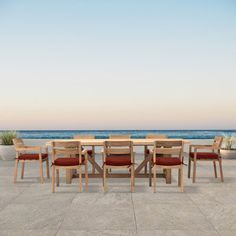 an outdoor dining table and chairs with the ocean in the background