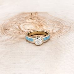 a gold ring with a blue band and a diamond in the center sits on a piece of wood