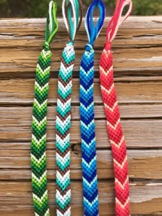 three bracelets with different colors and designs hanging from a wooden fence, one in the shape of an arrow