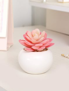 a small white vase with a pink flower in it sitting on a table next to other items