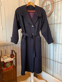 This sophisticated coat is made from heavier weight, 100 per cent pure virgin wool in classic navy blue. It has the original blue and gold buttons in the front and on the cuffs and shoulders; a matching tie belt and two front pockets, and is fully lined with thick purple blue satiny lining. The outside measurements, taken with the coat lying flat, are: shoulder to shoulder, 18 inches; armpit to armpit, 19 inches; sleeves, 23 inches; length, 49 inches; bottom edge, 30 inches. Please note that one of the front buttons is missing a bit of gold trim; also, the lining has some wear and discolouration at the bottom (see photos). Otherwise, the coat is in very good condition. Elegant Navy Peacoat With Double Button Closure, Elegant Navy Double-breasted Peacoat, Elegant Navy Double-breasted Outerwear, Elegant Navy Pea Coat With Button Closure, Navy Wool Elegant Coat, Navy Elegant Wool Coat, Elegant Navy Pea Coat For Workwear, Navy Elegant Pea Coat For Work, Elegant Navy Pea Coat For Work