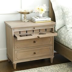 a wooden dresser sitting on top of a bed next to a white flower and a lamp