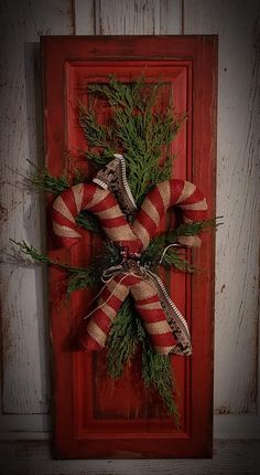 a red and white wreath hanging on the side of a wooden door with evergreen branches