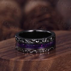 two wedding bands with purple and black enamel inlays on a wooden table top