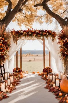 an outdoor wedding setup with candles, flowers and pumpkins on the side of the aisle