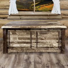 an old wooden table with curtains on the window sill in front of a rustic log cabin