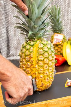 a person cutting up a pineapple on top of a table with bananas and peppers