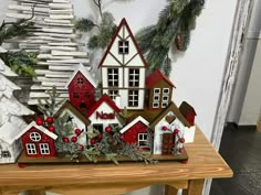 a wooden table topped with lots of christmas decorations next to a white and red house