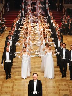 a man standing in front of a large group of people dressed in formal wear and tuxedos