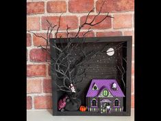 a halloween shadow box with a house and tree in the middle, on a shelf next to a brick wall