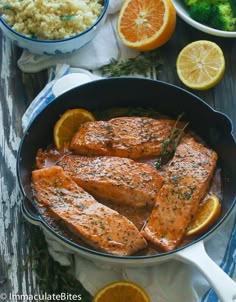 salmon in a skillet with oranges, rice and broccoli on the side