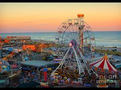 an amusement park next to the ocean with ferris wheel and rides on it at sunset