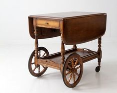 an old wooden cart with wheels and a table on it's back end, sitting against a white wall