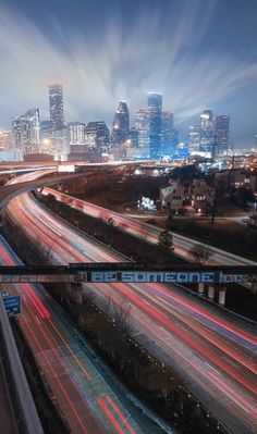 the city skyline is lit up at night with long exposure and light streaks on the road