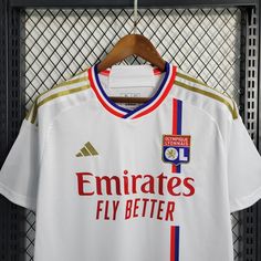 a soccer jersey hanging on a rack in front of a metal fence with the words emiratess fly better printed on it