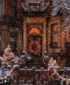 christmas wreaths are on the front steps of an old brick building with snow falling