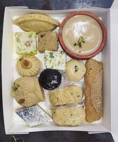 a box filled with assorted pastries next to a bowl of dip and sauce