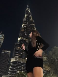 a woman is walking in front of the burj building at night, with her hand on her hip