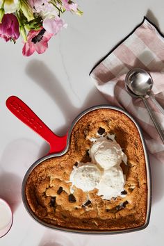 a heart - shaped cookie with ice cream in it next to a red spoon and pink flowers