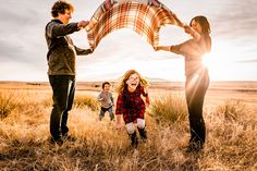 three people standing in a field, one holding a plaid blanket while the other is laughing