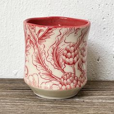 a red and white vase sitting on top of a wooden table next to a wall