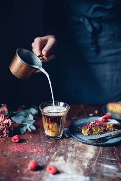 a person pouring something into a glass on top of a wooden table with raspberries